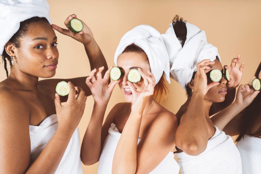 Happy young women wear white bathrobes head make cumbar facial teaspoon skin care mask eyes laughing together 1