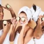 Happy young women wear white bathrobes head make cumbar facial teaspoon skin care mask eyes laughing together 1